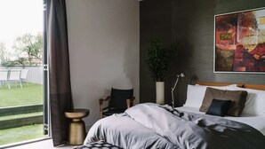 Habitación de hotel con cama, escritorio, una silla, planta en maceta y un cuadro abstracto grande en la pared.
