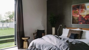 Ein Hotelzimmer mit einem Bett, einem Schreibtisch, einem Stuhl, einer Topfpflanze und einem großen abstrakten Gemälde an der Wand.