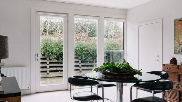 Una habitación con una mesa redonda de vidrio, sillas negras, una planta en maceta y vistas a un jardín a través de un ventanal corredero.