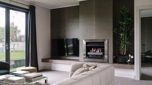 A modern living room with a fireplace, a television, and a large window. - Nephew Tim - 3 Bedroom Apartment (Daylesford)