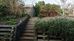 Eine Steintreppe führt zu einem hölzernen Tor, umgeben von verschiedenen Pflanzen und Sträuchern.