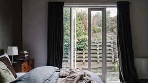 Un dormitorio con una cama, una mesita de noche, una lámpara y vistas a un área exterior con cerda de madera y vegetación.