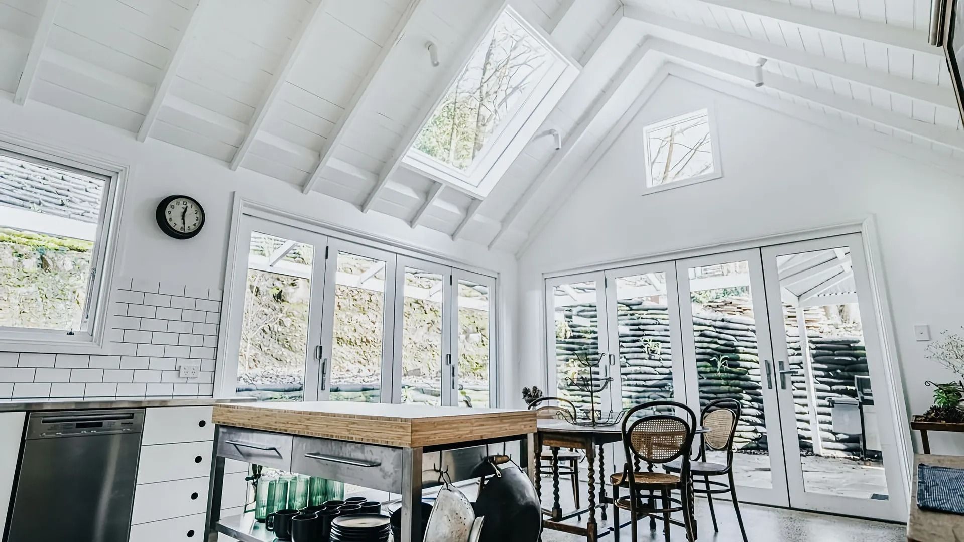 A bright kitchen with white walls, a wooden countertop, and a dining area with chairs.