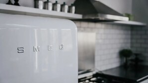 Keittiössä on valkoinen kodinkone, jossa on merkintä »SMEG», ja seinässä on laattapinta.