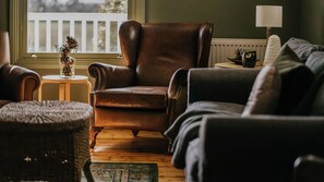 A cozy living room with a leather armchair, a grey sofa, and a small round table with a vase. - The Green Door-Renovated Miners Cottage with amazing views (Daylesford)