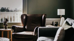 Una sala de estar acogedora con un sillón de cuero, una mesita redonda con una lámpara y vistas al exterior a través de una ventana.