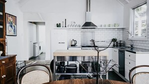 Una cocina moderna con armarios blancos, una isla central y un comedor con mesa y sillas de madera.