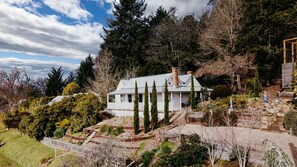 A white house with a gabled roof, surrounded by dense trees and a stone staircase leading up to the entrance. - The Green Door-Renovated Miners Cottage with amazing views (Daylesford)