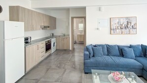 A modern kitchen with a built-in oven, a washing machine, and a dining area with a glass table and blue sofa. - Modern 1BR Apartment in Strovolos (Strovolos)