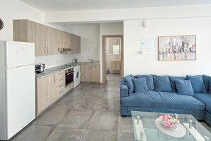 Cuina moderna amb forn integrat, rentadora i zona menjador amb taula de vidre i sofà blau.