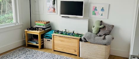 A child's playroom with a television, books, toys, and artwork on the wall.