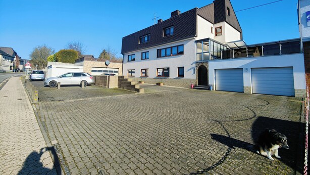 Ett bostadsområde med en asfalterad uppfart, ett tvåvåningshus med garage och en parkerad bil.