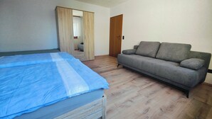Ett rum med en säng, en grå soffa och en garderob i trä.