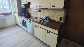Ett kök med en inbyggd ugn, en diskmaskin, en diskho och ett fönster med en gardin.