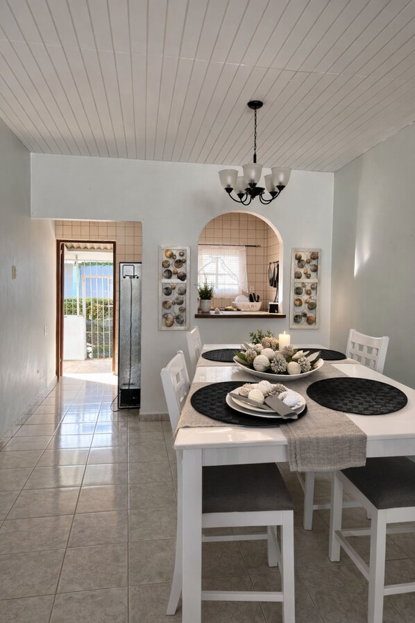 A dining area with a white table set for four, a chandelier, and a view of the kitchen through an archway.