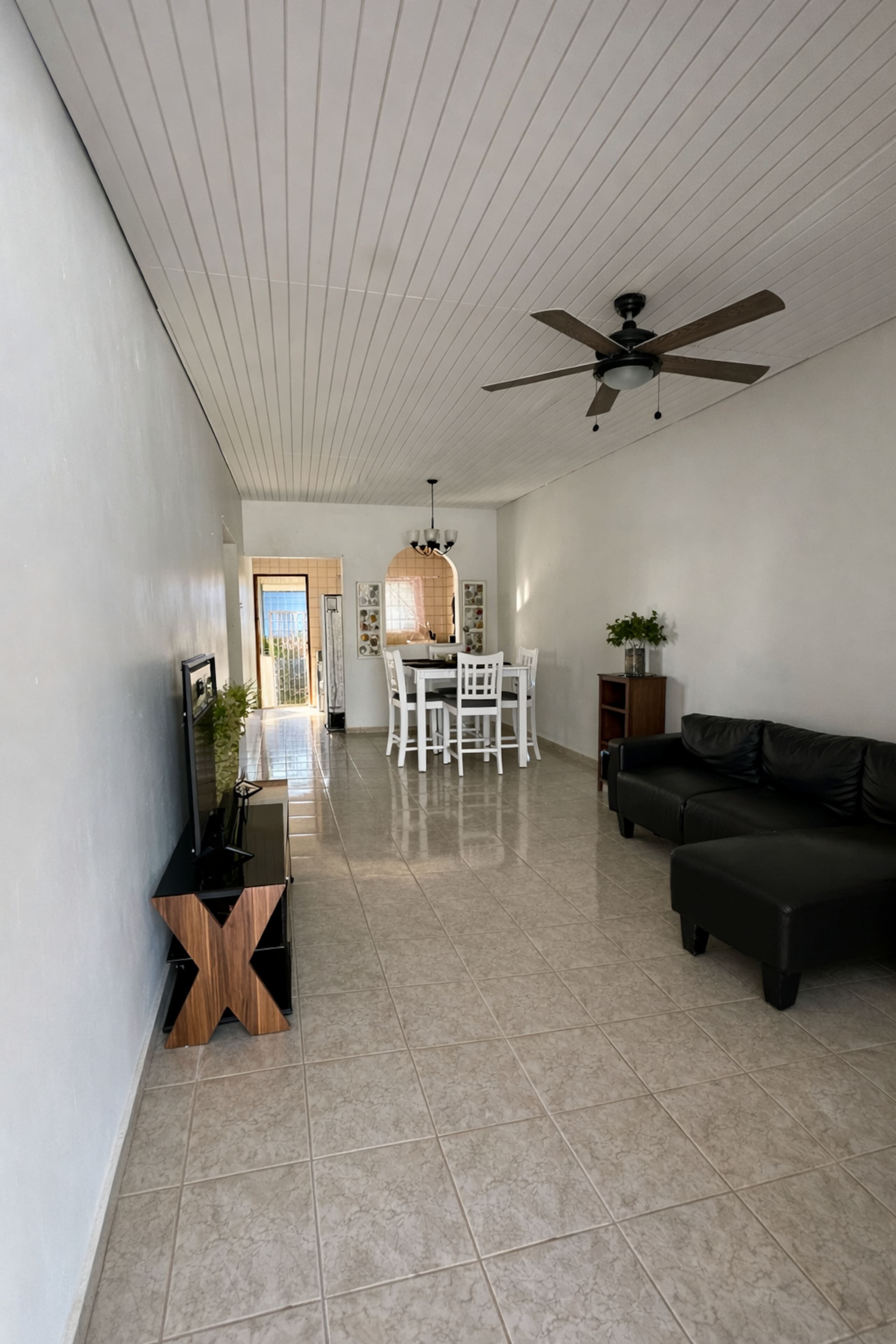 A spacious living area with a dining table and chairs, a sofa, and a ceiling fan.
