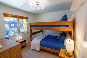 Ein Schlafzimmer mit Etagenbett, Schreibtisch, Stuhl, Nachttischlampe und einem Fenster mit Jalousien.