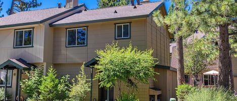 A two-story building with a stone facade, multiple windows, and a well-maintained garden with various shrubs and trees.