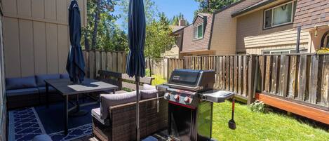 Un patio trasero con una parrilla, mobiliario exterior y un cerco de madera.