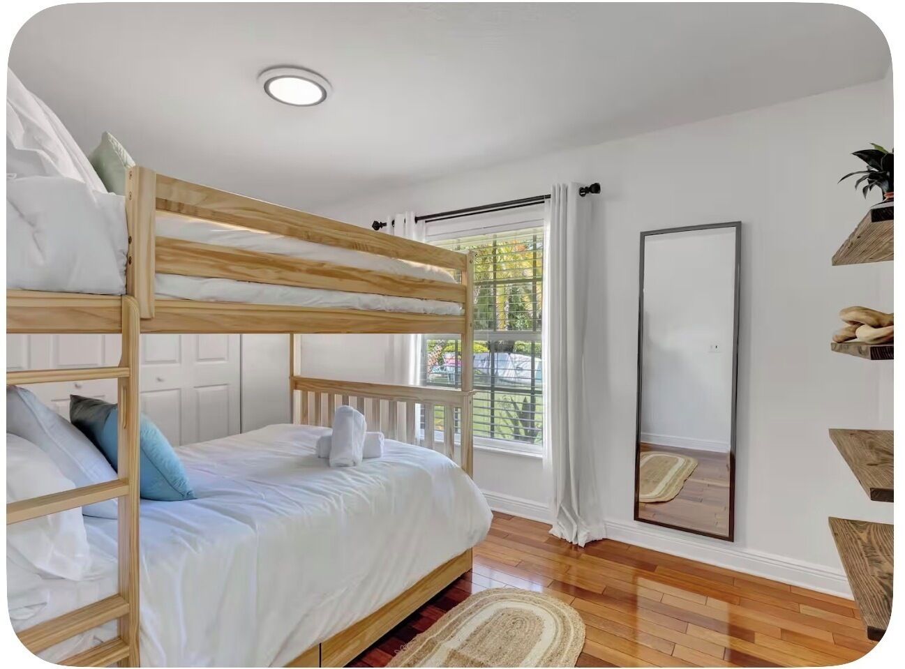 A bunk bed room with a window, a mirror, and wooden shelves.