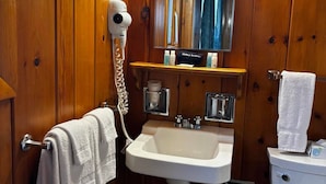 A wooden-paneled bathroom with a white sink, a hairdryer, a mirror, and a toilet. - Cozy 1BR hotel room, Hamilton - #342 Rode-A-Syde (Hamilton)