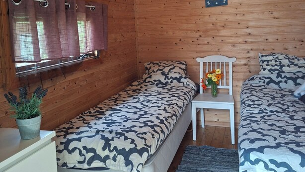 Una habitación de cabaña acogedora con dos camas, una mesita con un florero y una ventana con cortinas.