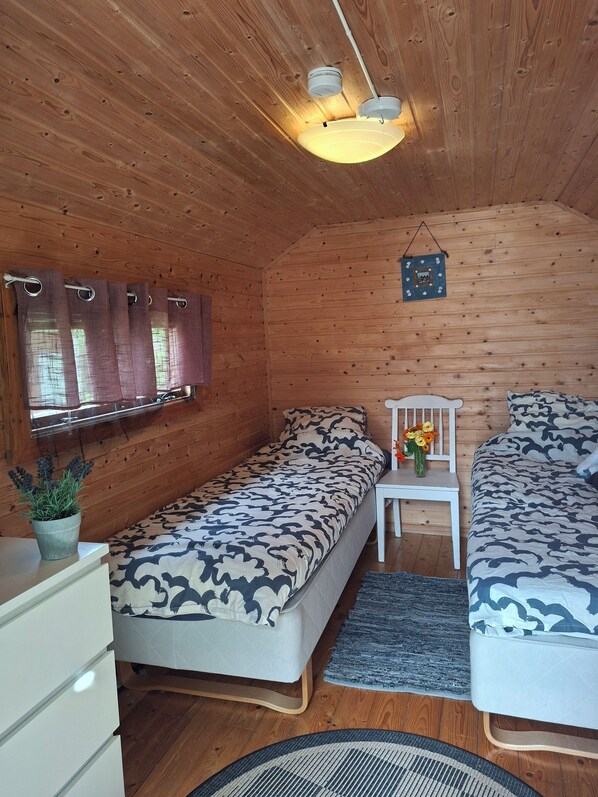 A cozy cabin room with two beds, a small table with a vase of flowers, and a window with curtains.
