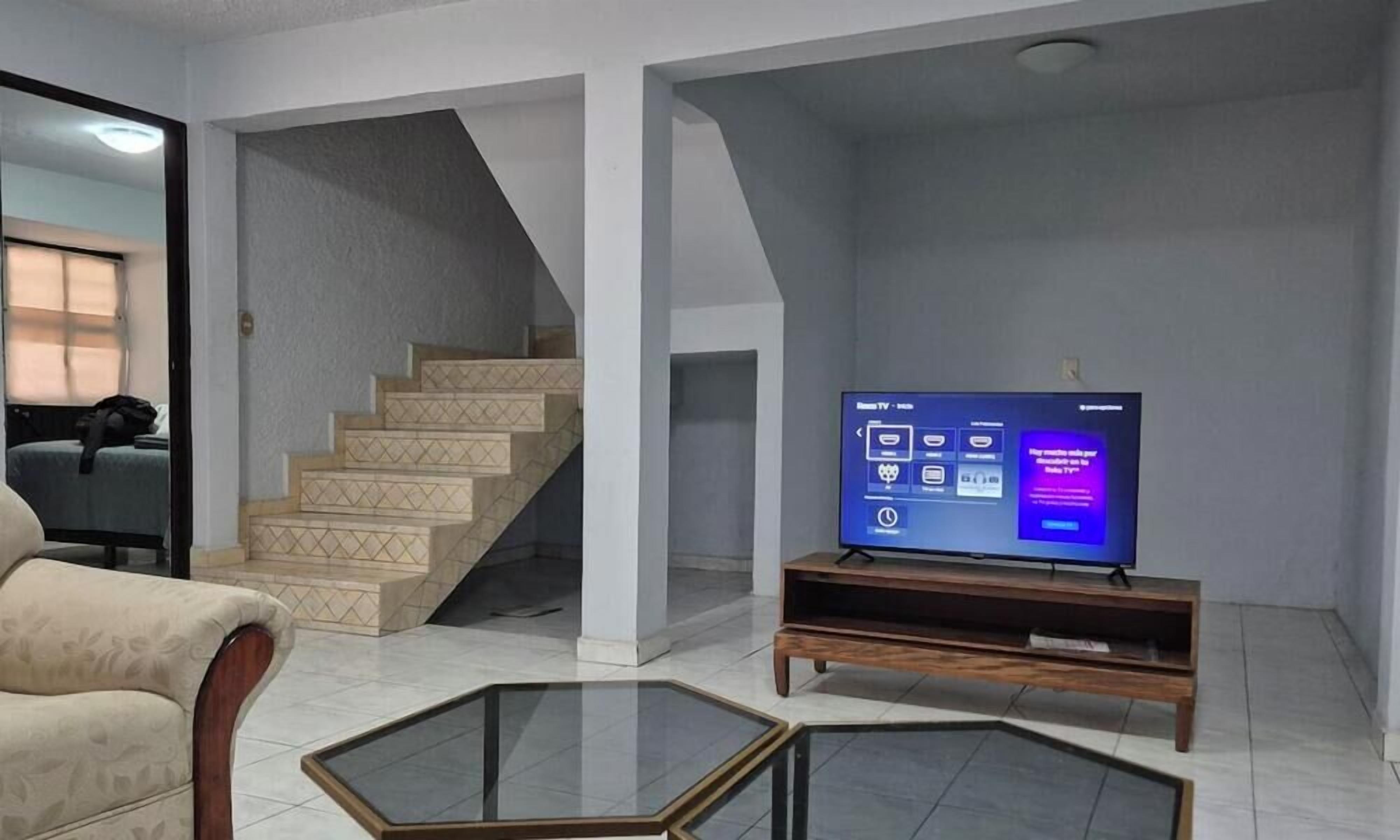 Una sala de estar con televisor, sofá, mesa de centro y escalera.
