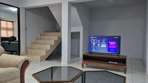 Een woonkamer met een televisie, een bank, een salontafel en een trap.