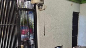 Een toegangspoort met een metalen hek, een luchtverkoeler aan de muur en een betegelde vloer.