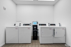 A laundry facility with four commercial dryers, a control panel, and a sign indicating 'Quality Vending Services.' - 🌊 GS Plantation East 2109 | Gulf View Condo | Resort Pools + Kiva Dunes Golf (Gulf Shores)