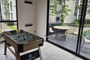 A foosball table in a modern indoor space with a glass wall offering a view of an outdoor patio area. - Departamento Maravillas (Guadalajara)