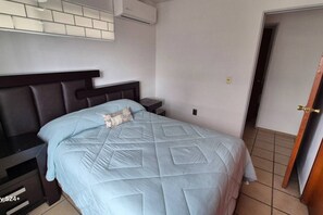 A bedroom with a bed, a nightstand, a wall-mounted air conditioner, and a door. - Casa ITESO cerca de la universidad y periferico (Tlaquepaque)