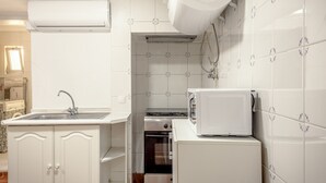 Una cocina compacta con un lavamanos, horno integrado, refrigerador blanco y aire acondicionado mural.