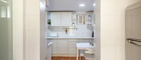 Una cocina estrecha con armarios blancos, encimera blanca y suelo de baldosas.