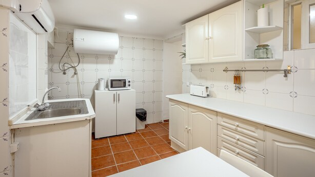 Cocina compacta con armarios blancos, un microondas, un tostador y un lavamanos.