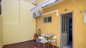 Un pequeño patio exterior con una mesa y sillas, un equipo de aire acondicionado y una puerta que da a un espacio interior.