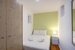 Een slaapkamer met een bed, nachtkastje, lamp en een houten garderobe.
