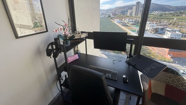 Ein Arbeitsplatz mit Schreibtisch, Stuhl und Blick auf eine Skyline durch ein großes Fenster.