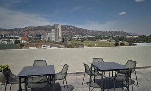 An outdoor terrace with tables and chairs, overlooking a cityscape with buildings and hills. - Depa Punto Sur 2 rec 2 baños alberca piso 9 (Santa Anita)