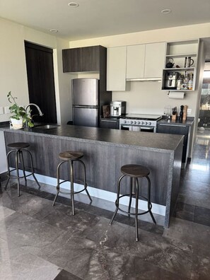 A modern kitchen with a central island, bar stools, a built-in oven, and a coffee machine. - Depa Punto Sur 2 rec 2 baños alberca piso 9 (Santa Anita)