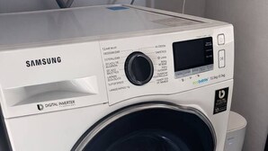 Eine Samsung Digital Inverter Waschmaschine mit Bedienfeld, Digitalanzeige und einem kleinen Mülleimer daneben.