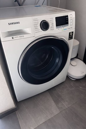 Eine Samsung Digital Inverter Waschmaschine mit Bedienfeld, Digitalanzeige und einem kleinen Mülleimer daneben.