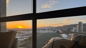 Ein Zimmer mit großem Fenster und Blick auf eine Stadtlandschaft bei Sonnenuntergang.