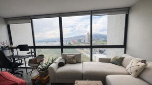 Ein modernes Wohnzimmer mit großem Fenster, einer Couch, einem Couchtisch und einem Schreibtisch mit Stuhl.