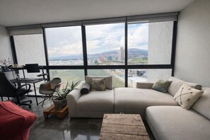 Ein modernes Wohnzimmer mit großem Fenster, einer Couch, einem Couchtisch und einem Schreibtisch mit Stuhl.