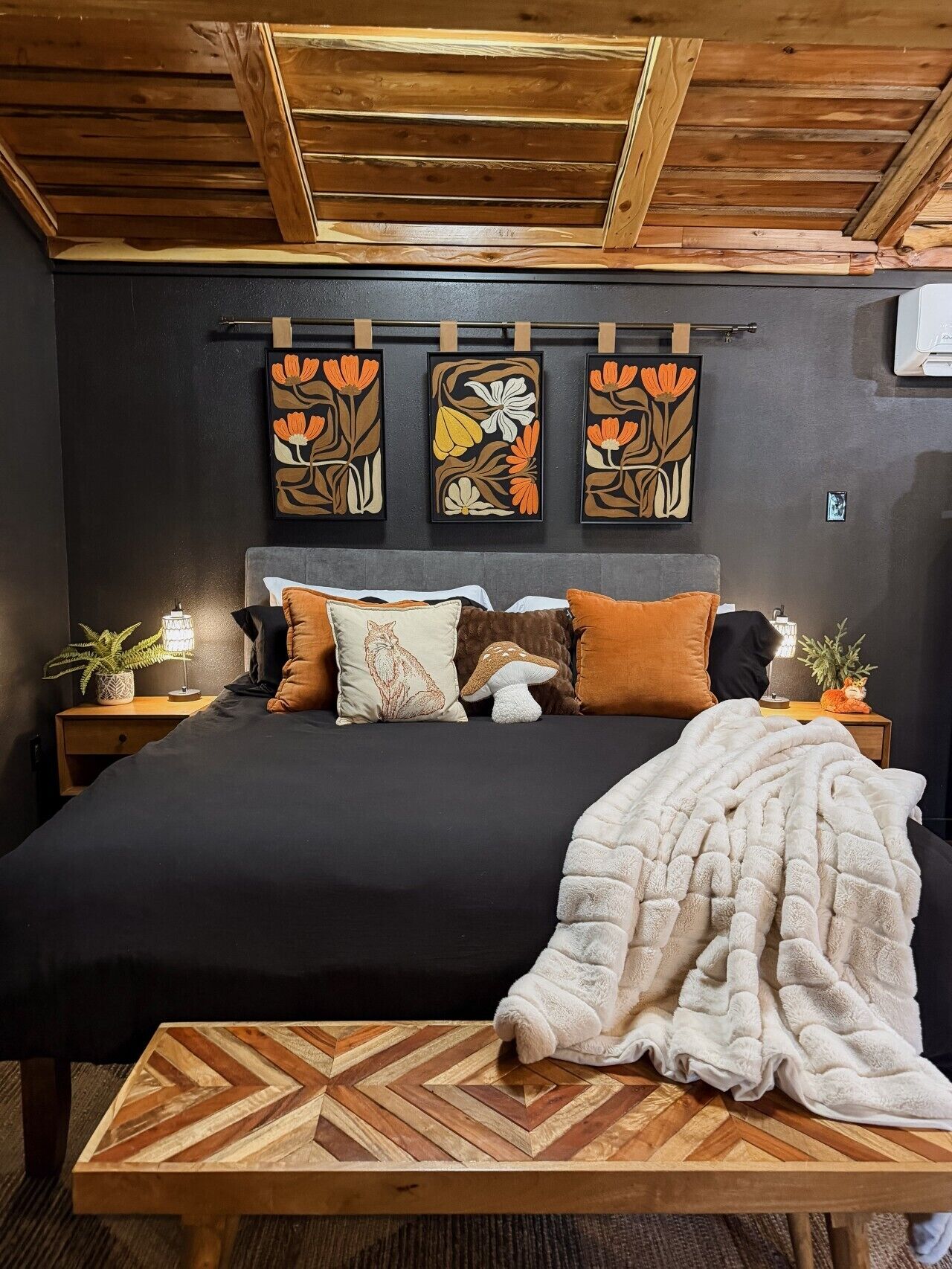 Une chambre à coucher avec un lit, des oreillers, une couverture, une tête de lit en bois et des œuvres d’art murales.
