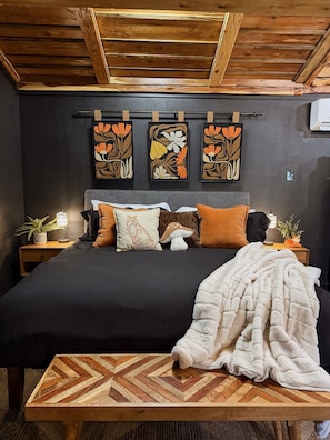 A bedroom with a bed, pillows, a blanket, a wooden headboard, and wall art. - Cedar Creek Crossing (all 4 units) (Mena)