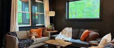 A cozy living room with two sofas, a coffee table, and a window with a view of greenery.