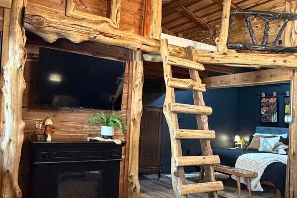 Un interior rústico con una escalera de madera, una cama y una chimenea.
